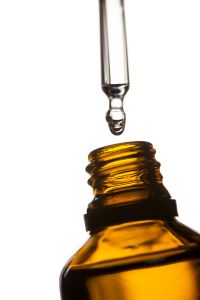 Gota de óleo de canabinol caindo de dosador para frasco de cor âmbar