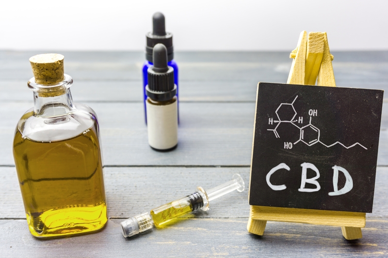 Frascos e seringas sobre uma mesa ao lado de lousa com a estrutura molecular do CBD